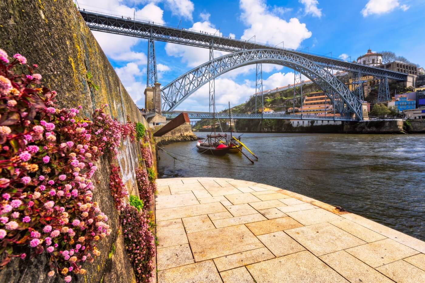 Vista sul fiume Douro a Porto, con una barca tipica ormeggiata e il Ponte Dom Luís I che si staglia nel paesaggio urbano.