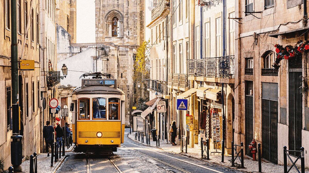 Tram giallo storico che attraversa le stradine acciottolate di Lisbona, con la Cattedrale di Sé sullo sfondo.