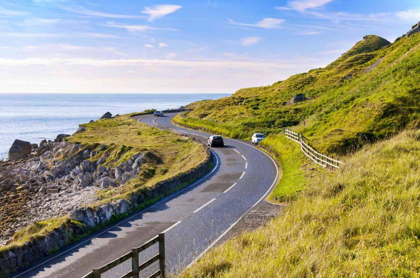 Strada costiera in Irlanda con auto che guidano sulla sinistra, circondate dalla natura.